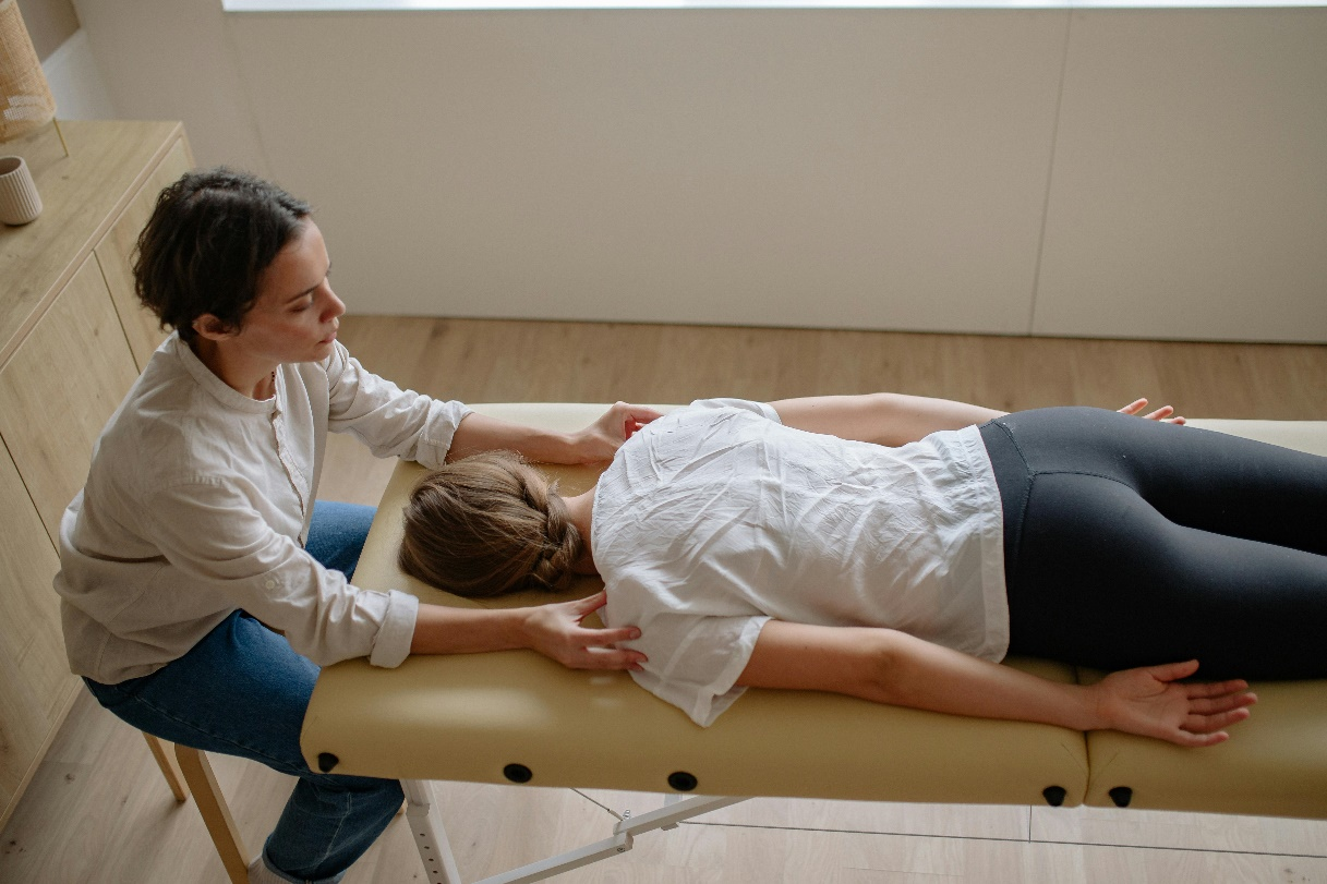 A woman in a white shirt lying down on a massage bed and getting her shoulders examined